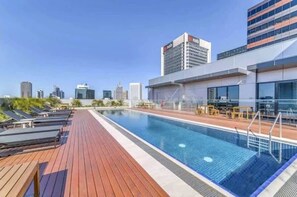 Ein Pool auf dem Dach mit Liegestühlen und einer Skyline im Hintergrund.