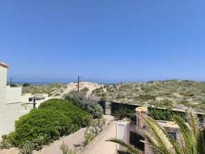 Eine Küstenlandschaft mit blauem Himmel, einem Weg, der zu einem Gebäude mit einer Tür führt, und einem Blick auf das Meer in der Ferne.