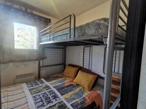 Ein Mehrbettzimmer mit Fenster, Heizkörper und einer gestreiften Decke auf dem unteren Bett.