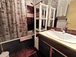 Ein Badezimmer mit einem weißen Waschbecken, dunklen Fliesenwänden, einem Duschvorhang mit Meeresmotiven und einem weißen Handtuchhalter.