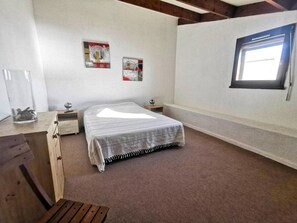 Ein Schlafzimmer mit Bett, Fenster, Nachttisch und einem an der Wand hängenden Bild.