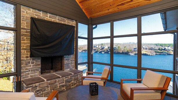 A stone fireplace, a TV mounted on the wall, and a view of a lake. - Luxurious High End Family Friendly Lake House. Dock, Floats, 10 min to Trident. (Crane Hill)