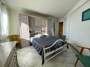 A bedroom with a bed, wardrobe, chair, and a small table. - Sea view apartment with parking - 4 guests (Cap d'Agde)