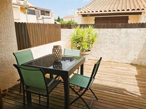 Eine Terrasse im Freien mit einem Glastisch, grünen Stühlen, einem Blumentopf und einem Holzzaun.