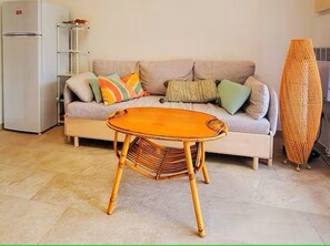 Ein Wohnzimmer mit einer Couch, einem kleinen Tisch, einem Heizlüfter und einem Kühlschrank.