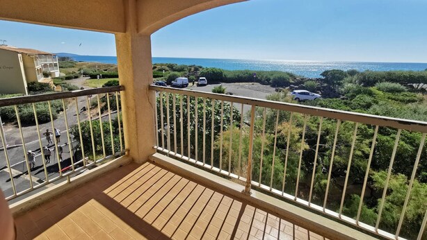 Een balkon met uitzicht op zee, een geplaveid terras en een gebouw met de tekst 'Conquer'.