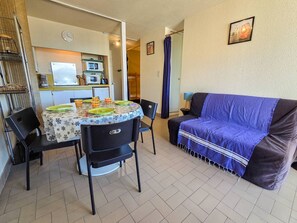 Ein kompakter Wohnbereich mit Esstisch, Stühlen, einer Couch, einer Küchenzeile und einer Duschgelegenheit.