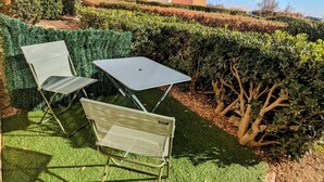 A patio area with two chairs and a table, surrounded by neatly trimmed hedges and a small tree. - 2-room apartment, parking - 4 guests, sea view (Cap d'Agde)