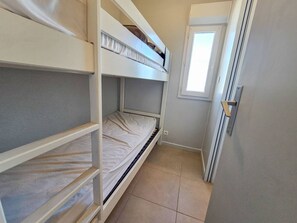 Ein schmales Zimmer mit Etagenbetten, einer Tür und einem Fenster.