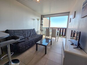 Ein modernes Wohnzimmer mit einer Couch, einem kleinen Tisch, einem Fernseher und einem Balkon mit Blick.