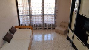 Una camera da letto con un letto, una sedia, un piccolo divano, una TV e una finestra con tende.