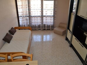 A bedroom with a bed, a chair, a small sofa, a TV, and a window with curtains. - Studio for 2 guests near beach - Cap d'Agde (Cap d'Agde)