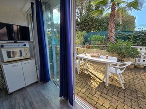 Eine Küchenzeile mit einer Mikrowelle, ein Essbereich mit Tisch und Stühlen und Blick auf den Garten durch eine Glastür.