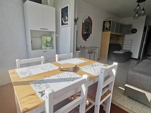 Ein Essbereich mit Holztisch und weißen Stühlen, eine Küche mit weißen Schränken und ein graues Sofa im Hintergrund.