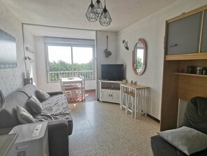 Ein Wohnzimmer mit Sofa, Fernseher, Balkon und Essbereich.