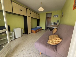Ein kompakter Raum mit Bett, einer Schlafcouch, einer Küchenzeile und einem kleinen Tisch.