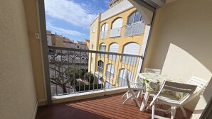 A balcony with a table and chairs, a view of buildings, and a railing. - Studio in Cap d'Agde, AC - 4 guests, near beach (Cap d'Agde)