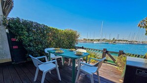 Terraza de madera con mesa y sillas, con vista a un puerto deportivo lleno de veleros.