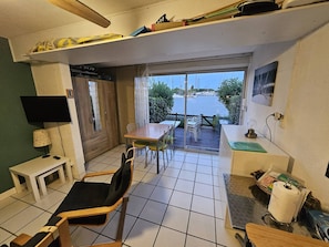 Ein gemütlicher Raum mit Esstisch, Stühlen, einem kleinen Fernseher und Blick auf das Wasser.