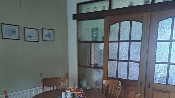 A dining area with a round wooden table, four wooden chairs, a wicker basket with bananas, and a window with patterned glass. - House Sleeps 2 With Garden and Parking (Dublin)