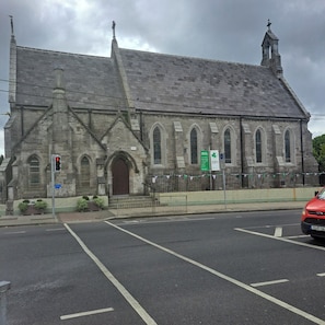 A historic stone building with a prominent entrance, multiple windows, and a steeple.