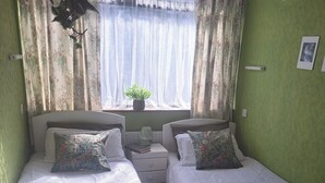 A twin room with two single beds, a bedside table with a book, a potted plant, and a window with sheer curtains. - House Sleeps 2 With Garden and Parking (Dublin)