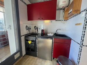 A compact kitchen with a stove, oven, sink, and red cabinets. - Apartment near naturist area - 6 guests (Cap d'Agde)