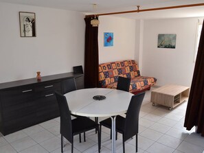 Ein Essbereich mit einem runden Tisch, schwarzen Stühlen, einem dunklen Schrank und einem farbenfrohen Sofa.