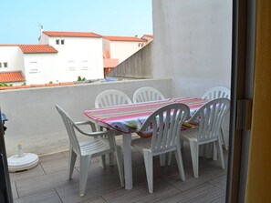 Ein Balkon mit Tisch und Stühlen, Blick auf Gebäude mit roten Dächern und einem klaren Himmel.