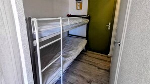 Quarto com beliche, uma janela pequena, porta e termostato na parede.