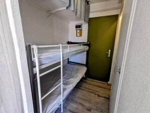 Ein Schlafraum mit Etagenbetten, einem kleinen Fenster, einer Tür und einem Thermostat an der Wand.