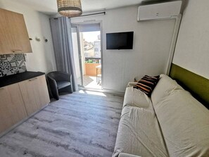 Ein gemütliches Zimmer mit einer Schlafcouch, einem Sessel, einem kleinen Tisch, einem Fernseher und einer Klimaanlage.