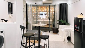 A modern hotel room with a round table, two bar stools, a sofa, a bed, a washing machine, a refrigerator, and a decorative partition with a patterned design. - Àla Homestay District 10 Apartment (Ho Chi Minh City)