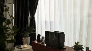 A living room with a television on a wooden stand, a patterned rug, a small table with a candle, and a potted plant. - Àla Homestay District 10 Apartment (Ho Chi Minh City)