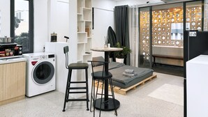 A compact living space with a washing machine, a dining table with chairs, a small sofa, and a decorative partition with circular cutouts. - Àla Homestay District 10 Apartment (Ho Chi Minh City)