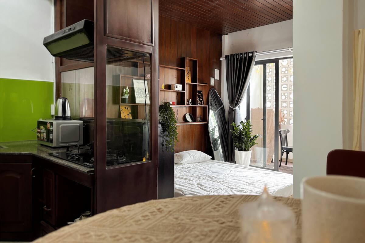 A hotel room with a kitchenette, a bed, a window with curtains, and a view of the outside.