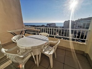 Ein Balkon mit rundem Tisch und Stühlen, Blick aufs Meer und Gebäude im Hintergrund.