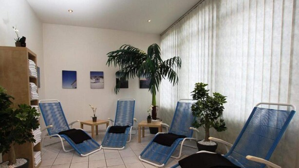A room with four blue lounge chairs, a large potted plant, a wooden shelf with towels, and a wall with framed pictures. - 2 Person Holiday Park Home in Neu-isenburg (Neu-Isenburg)
