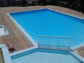 Ein rechteckiger Schwimmteich mit einer Metallleiter und einer gefliesten Terrasse darum.