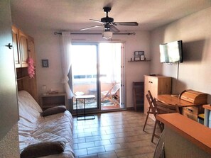 Ein Zimmer mit einem Bett, einem Schreibtisch, einem Sessel, einem Fernseher und einem Deckenventilator.