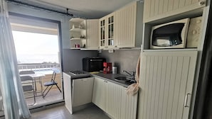 A compact kitchen with a microwave, sink, and a small refrigerator. There is a dining area with a table and chairs visible through an open door. - Studio with AC, sea view - 4 guests (Cap d'Agde)