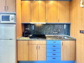 A kitchen with wooden cabinets, a microwave, a stove, and a sink. - Comfortable 2-bedroom apartment 100m from the beach, air conditioning, balcony, satellite TV. (Roses)