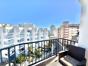 A balcony with a wicker sofa, a view of multi-story buildings, and a clear blue sky. - Comfortable 2-bedroom apartment 100m from the beach, air conditioning, balcony, satellite TV. (Roses)