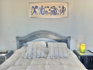 A bed with a patterned headboard, two pillows, a bedside table with a lamp, and a wall-mounted artwork. - Comfortable 2-bedroom apartment 100m from the beach, air conditioning, balcony, satellite TV. (Roses)