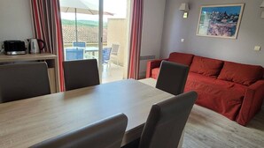Een kamer met een eettafel, stoelen, een rode bank, een schilderij aan de muur en uitzicht door een raam.