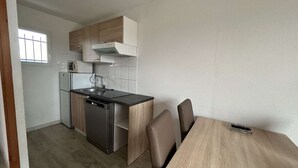 Een praktische keuken met een vaatwasser, een magnetron en een fornuis. Er is een eettafel met stoelen en een raam met roedeijzers.