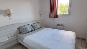 Een slaapkamer met een bed, twee nachtkastjes, een wandlamp, een raam met gordijnen en een radiator.