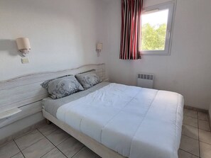 Ein Schlafzimmer mit einem Bett, zwei Nachttischen, einer Wandlampe, einem Fenster mit Vorhängen und einer Heizung.