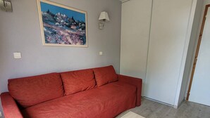 Een rode bank, een houten salontafel, een schilderij aan de muur en een witte deur.
