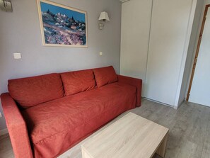 Ein rotes Sofa, ein Holztisch, ein Bild an der Wand und eine weiße Tür.
